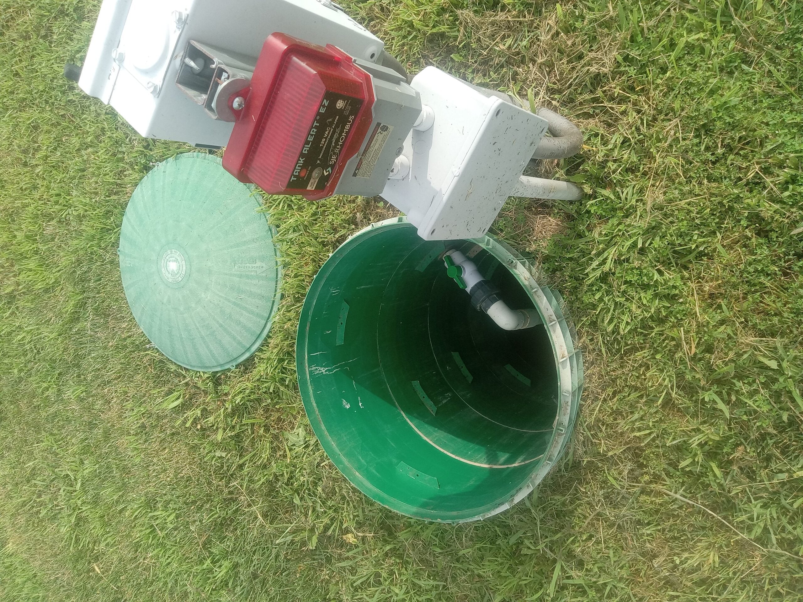 SJE Rhombus Tank Alert EZ alarm system above an open septic tank with green lid nearby.