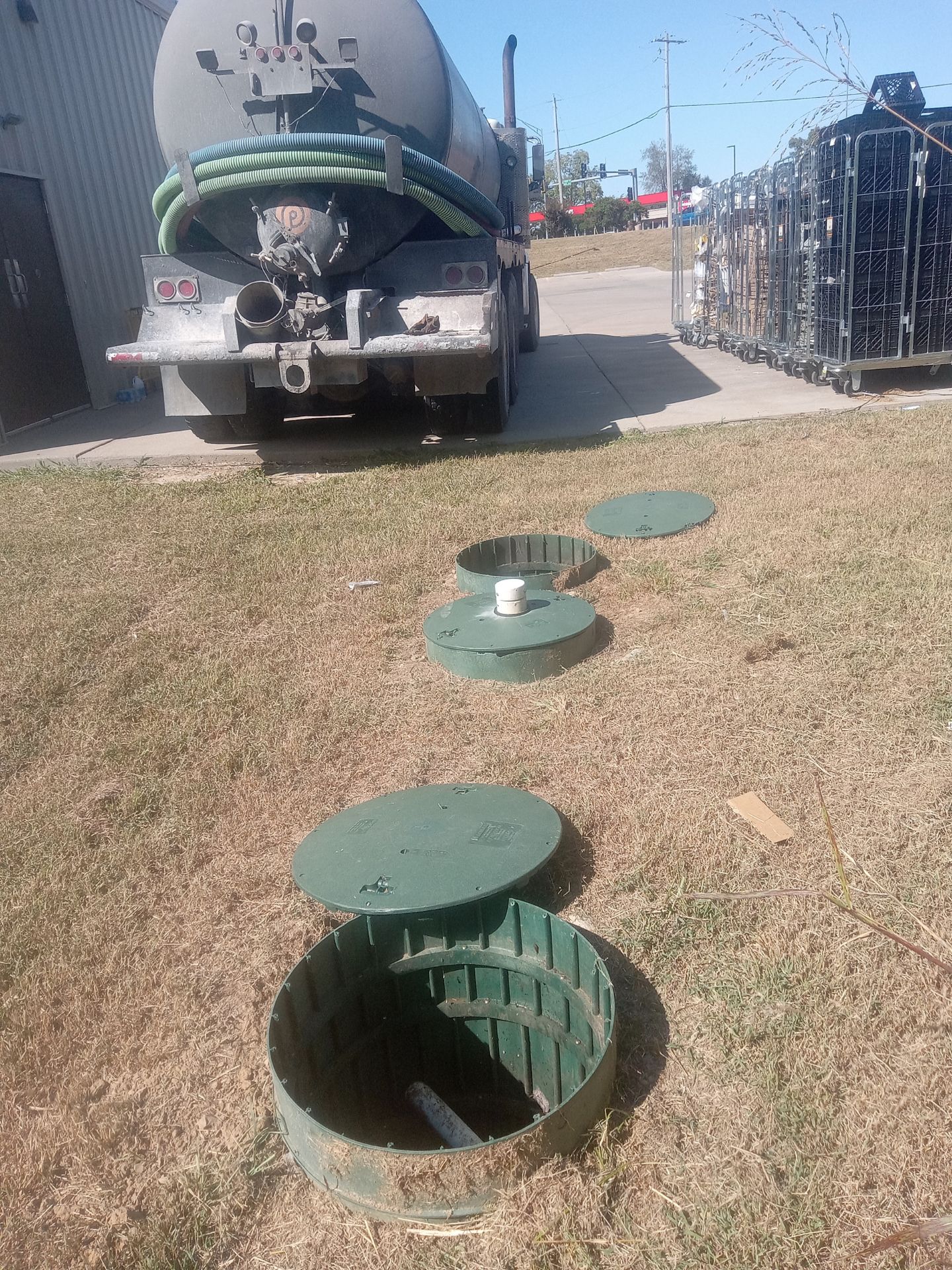 Septic truck at site with multiple green septic tank access lids and open tank.