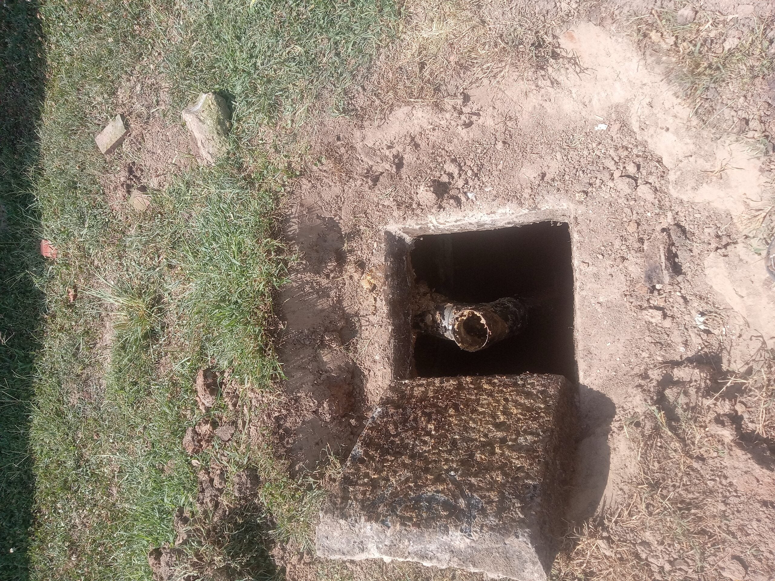 Open drain pipe with debris inside, surrounded by dirt and grass.