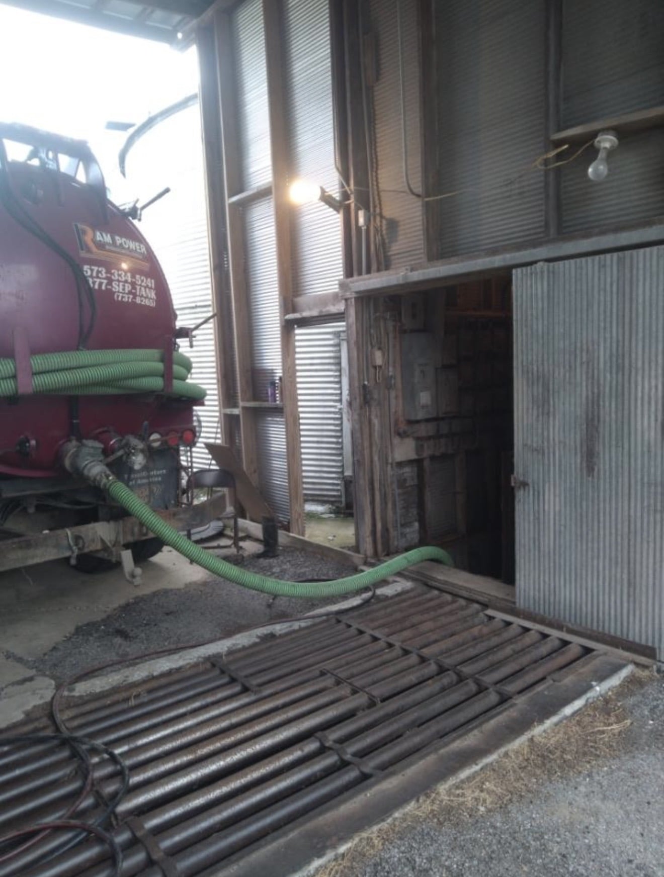 Red septic tank truck with green hose filling a pit inside a barn.